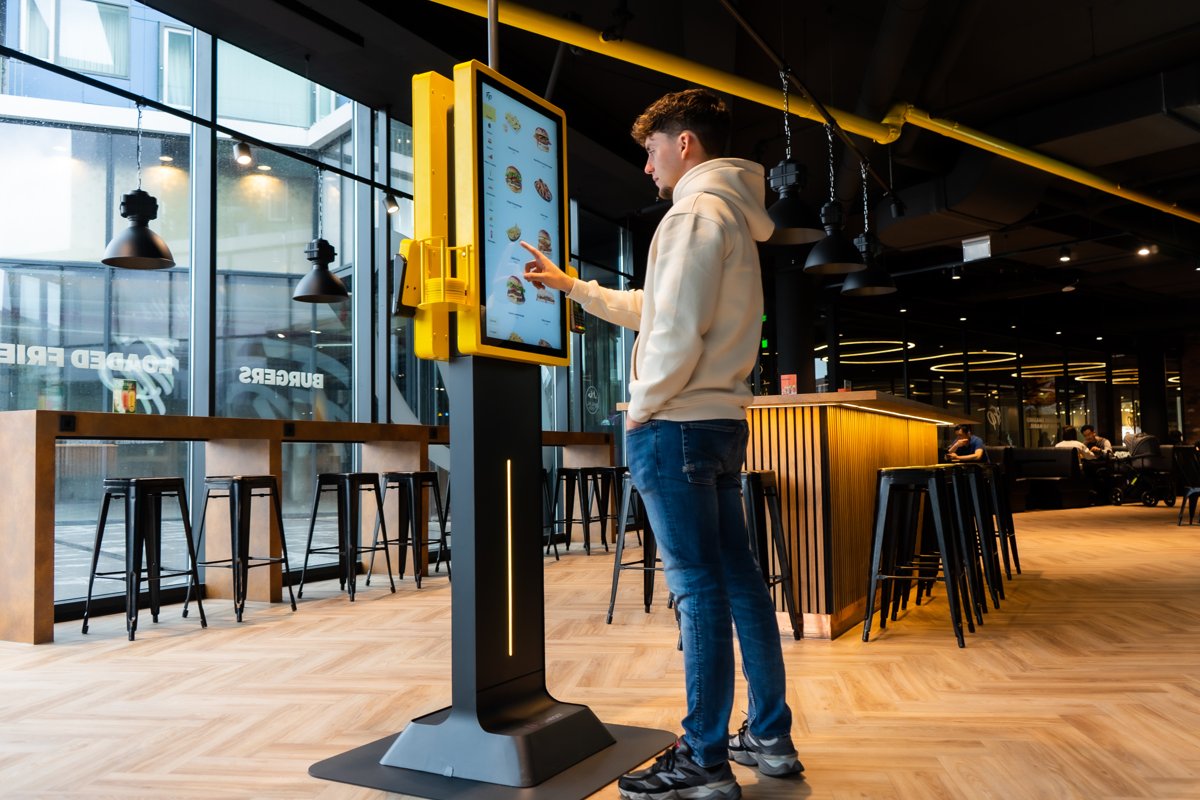 Client qui commande sur une Borne Onesix jaune avec un grand écran tactile dans un restaurant de burgers