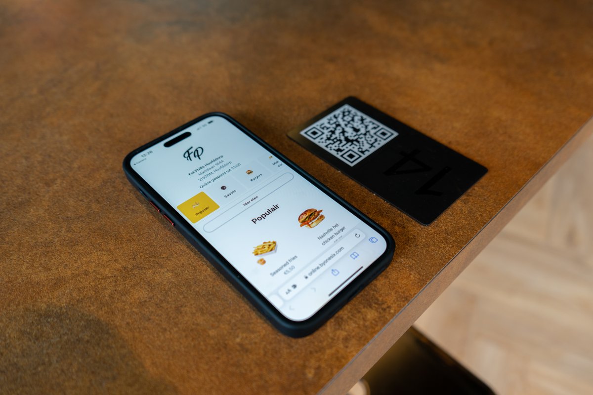 Téléphone affichant la carte digitale de l'Online Kiosk à côté d'un chevalet QR sur une table