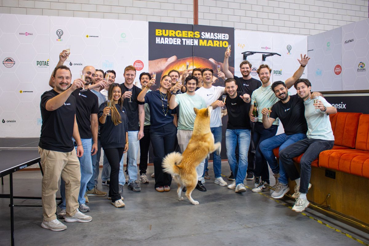 L’équipe Onesix lève son verre de champagne dans les bureaux d’Onesix, avec un chien qui saute au premier plan
